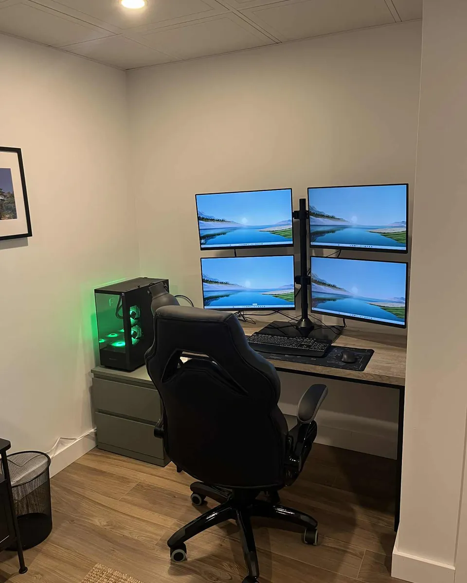 Poste de trading installé chez un client avec quatre écrans sur support articulé et tour noire à éclairage vert.